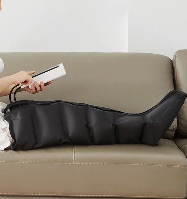 femme avec télécommande dans les main bottes pressothérapie sur sofa beige fond blanc 