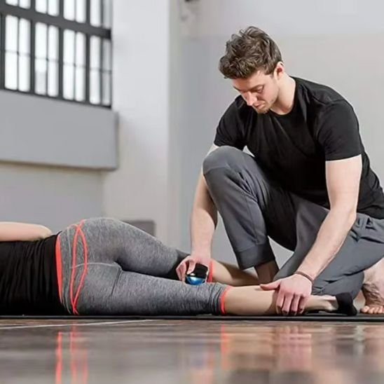 homme en teeshirt noir et pantalon-gris boule de massage sur femme en pantalon gris dans un gymnase