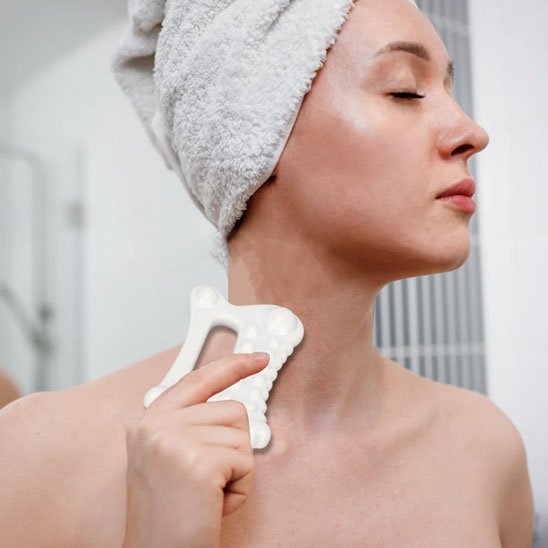 femme une serviette sur la tête avec un gua sha sur son cou dans la salle de bain