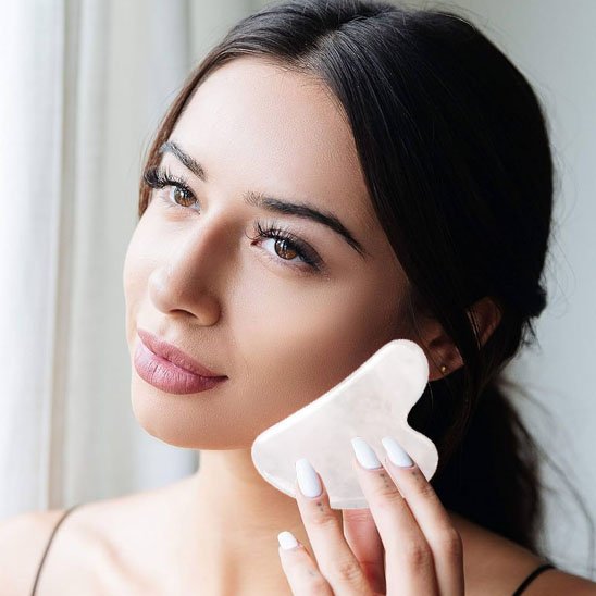 gua sha sur la joue devant une fenêtre