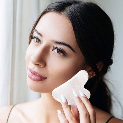 gua sha sur la joue devant une fenêtre