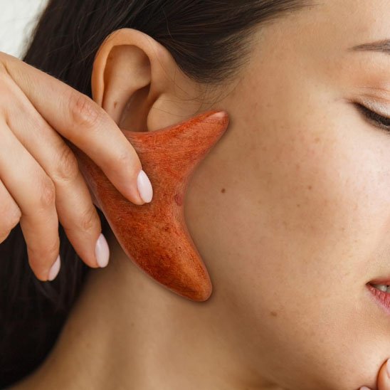 main avec ongle blanc sur gua sha en bois sur le visage 