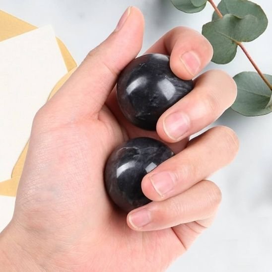 main tiens deux boule de massage noir sur fond feuille vert