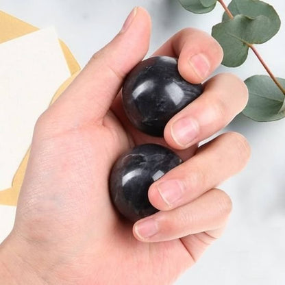 main tiens deux boule de massage noir sur fond feuille vert