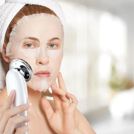 Masseur visage sur femme avec un masque facial devant une fenêtre