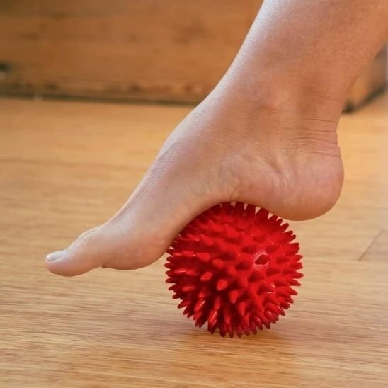 pied sur boule de massage rouge sur plancher bois