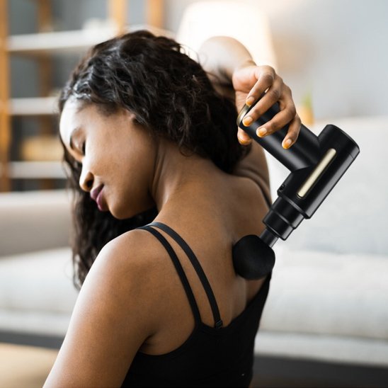 femme en noir avec pistolet de massage dans le salon 