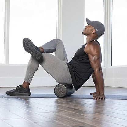 homme en camisole noir et pantalon gris rouleau de massage noir devant grande fenêtre