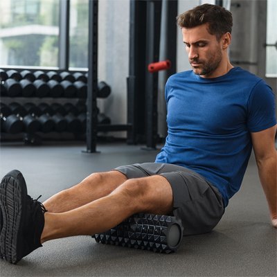 homme en gilet bleu assis sur rouleau de massage noir dans un gymnase