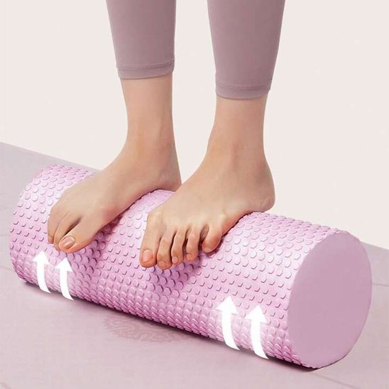 Pieds de femme en pantalon rose sur rouleau de massage rose tapis gris fond blanc