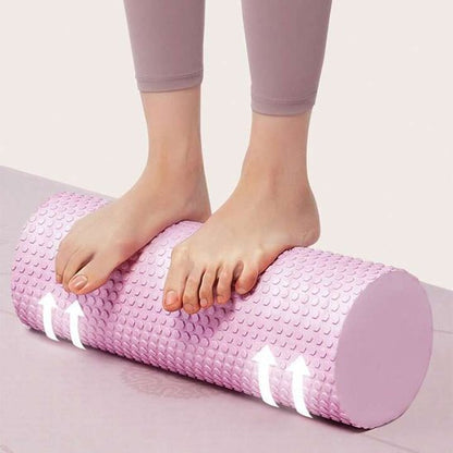 Pieds de femme en pantalon rose sur rouleau de massage rose tapis gris fond blanc
