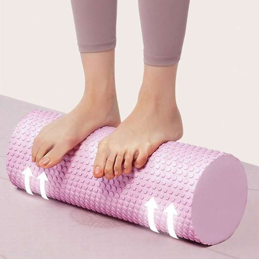 Pieds de femme en pantalon rose sur rouleau de massage rose tapis gris fond blanc