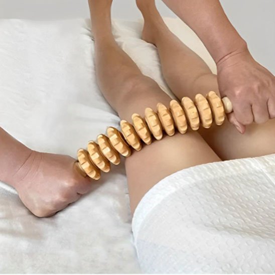 main sur rouleau de massage bois sur cuisse  dans une sale de massage