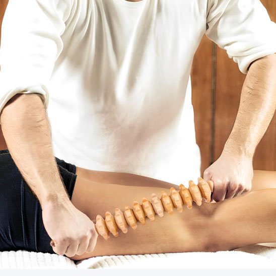homme en gilet blanc avec rouleau de massage bois sur cuisse dans un salon de massage