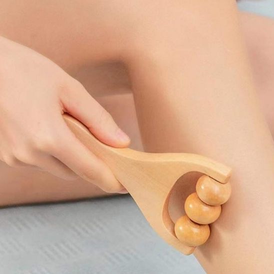 Main sur rouleau de massage en bois lisse sur jambe et mollet fond flou