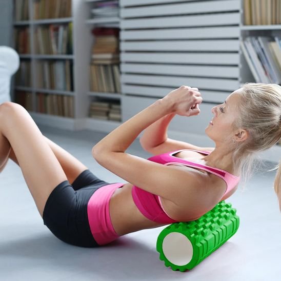 Femme en camisole rose short noir et rose sur rouleau massage vert fond flou