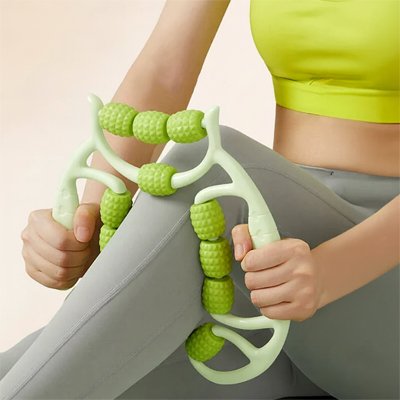 Main jambe de femme en camisole vert et pantalon gris avec rouleau massage cellulite vert sur fond blanc