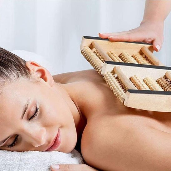 main de  femme avec rouleaux de massage en bois sur table de massage