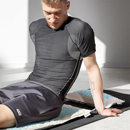 homme assis sur tapis d'acupression sur le plancher d'un appartement vide